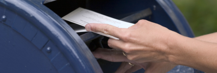 person putting mail in into blue mailbox